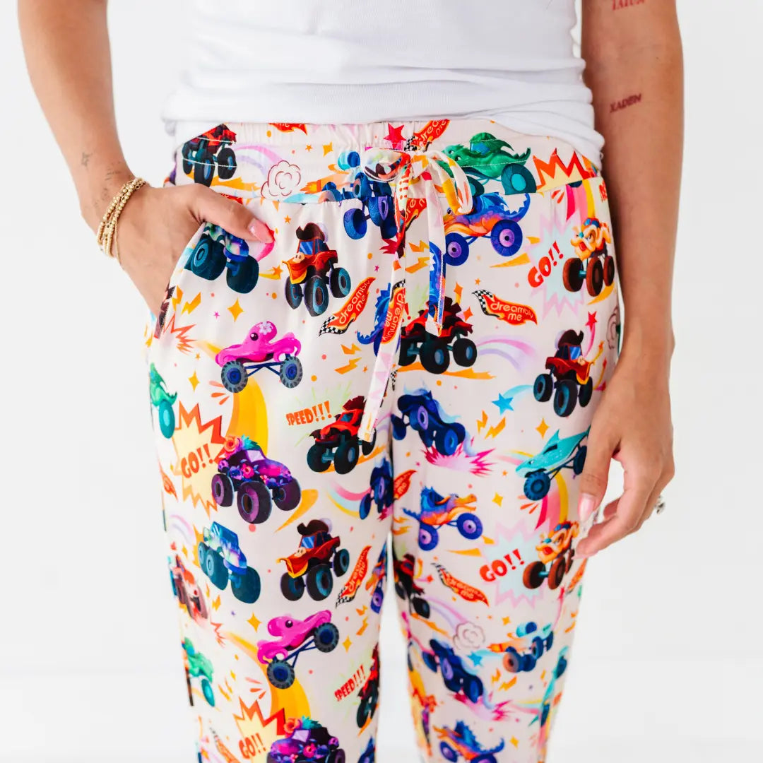 Close-up of women's pajama pants with a drawstring waist and a colorful monster truck print, one hand in the pocket.